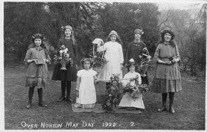 Garland and flower baskets at Over Norton, May Day 1922. The garland is hung from a pole by the two attendants at the front. Note the girls at left and right, holding money boxes.