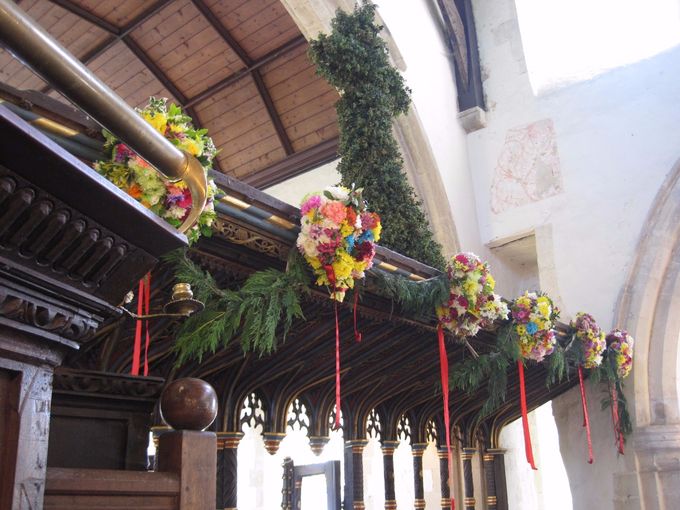 Charlton-on-Otmoor - garlands hang above the rood screen, strung together on a rope festooned with greenery. The leafy cross above remains there all the year round (photo Tim Healey).